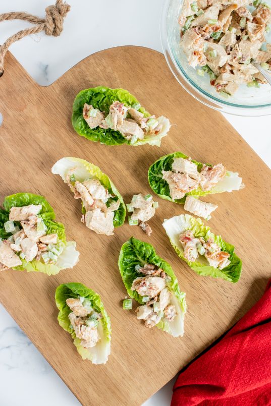 Lots of lettuce leaves filled with a creamy chicken salad and served on a wooden chopping board