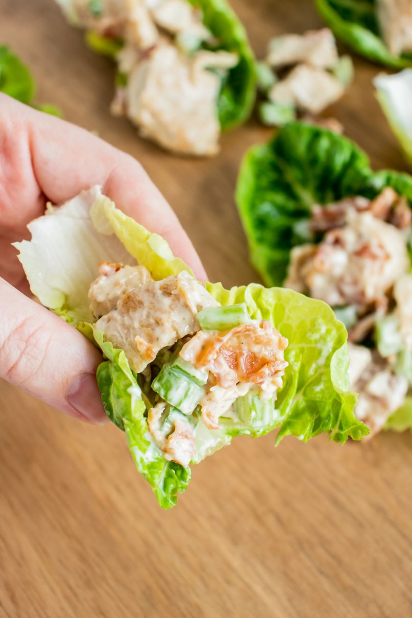 Creamy chicken salad served in a lettuce leaf with a hand holding it and a bite having been taken