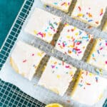 overhead shot of a cake topped with icing and sprinkles and cut into squares resting on a wire rack