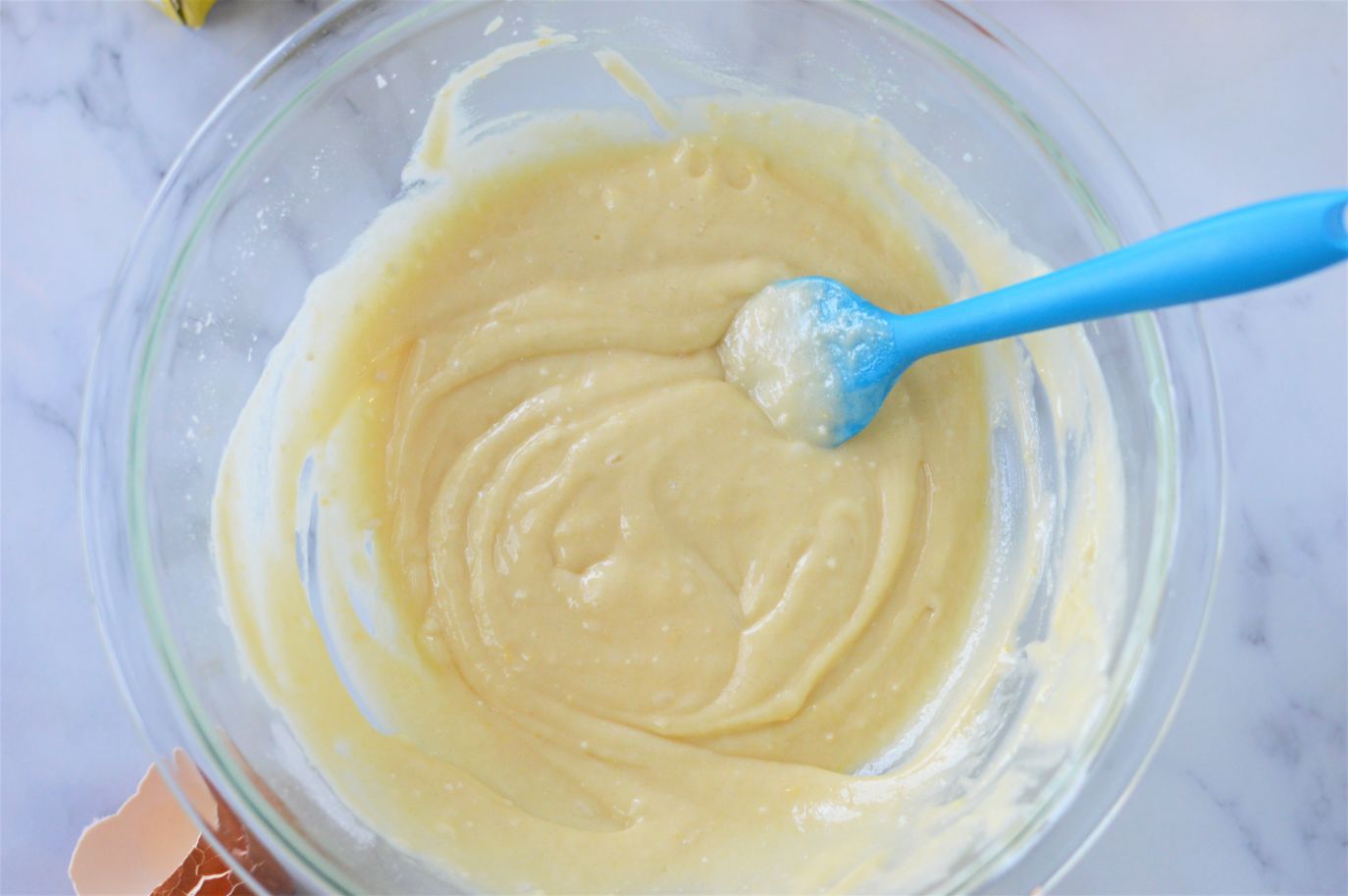 A large glass bowl full of pancake mix muffin batter being stirred by a blue silicone spatula