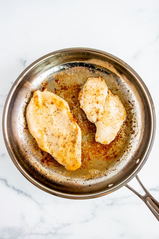 a chicken breast sliced in half and being cooked in a saucepan