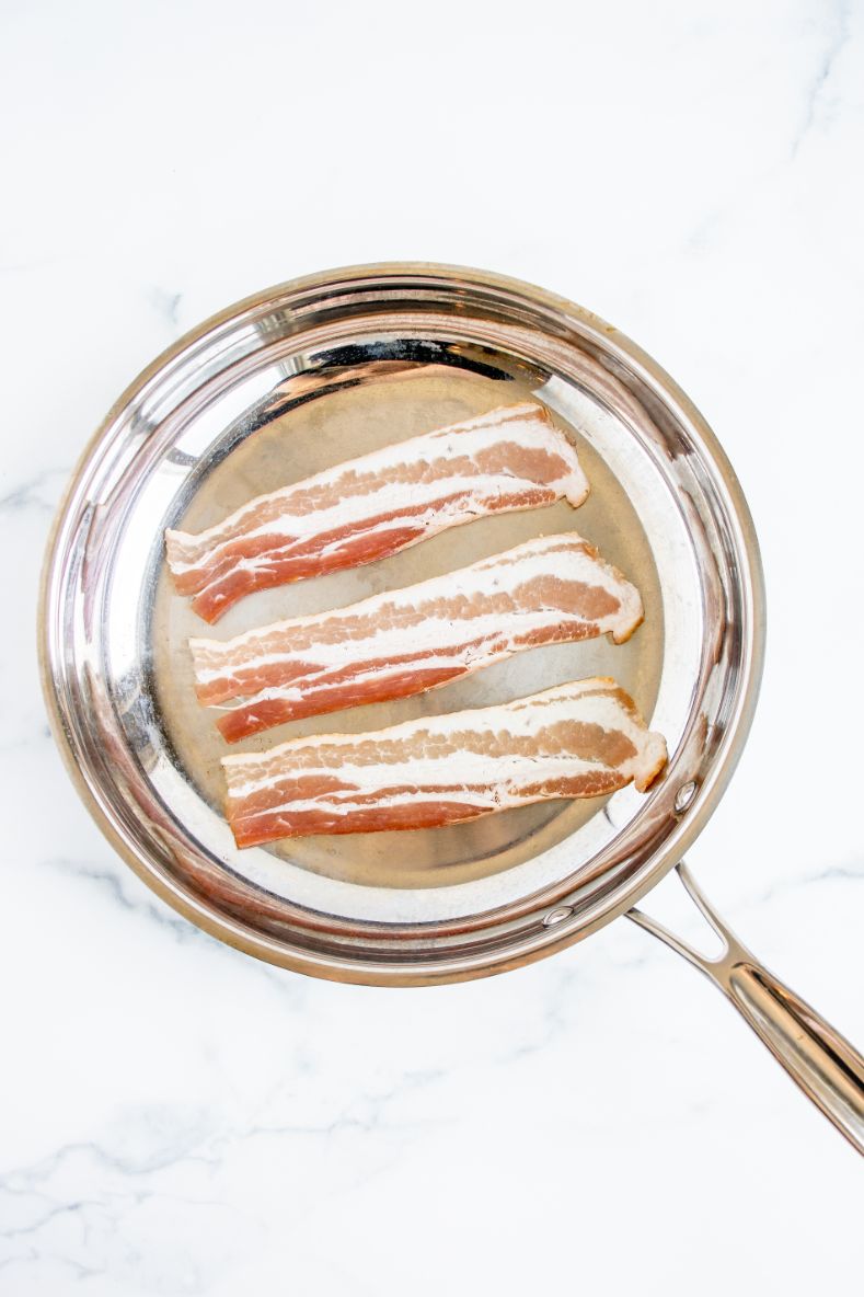 3 slices of bacon cooking in a saucepan