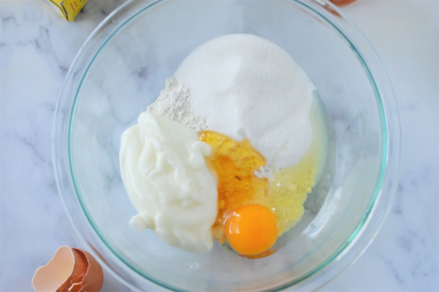 overhead shot of pancake mix, yogurt, sugar, egg and honey in a large glass bowl