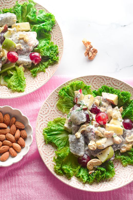 Overhead shot of a savory fruit salad served on a bed of lettuce with a side of almonds