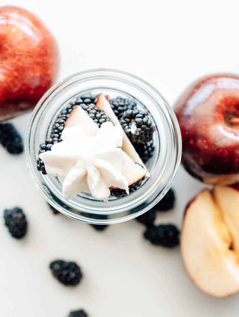 Apples and blueberries beside a mason jar filled with blackberries and yogurt