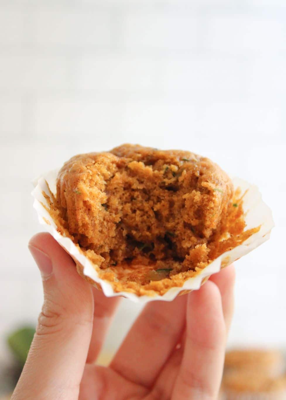A pumpkin muffin served in a white muffin liner being held up by a hand