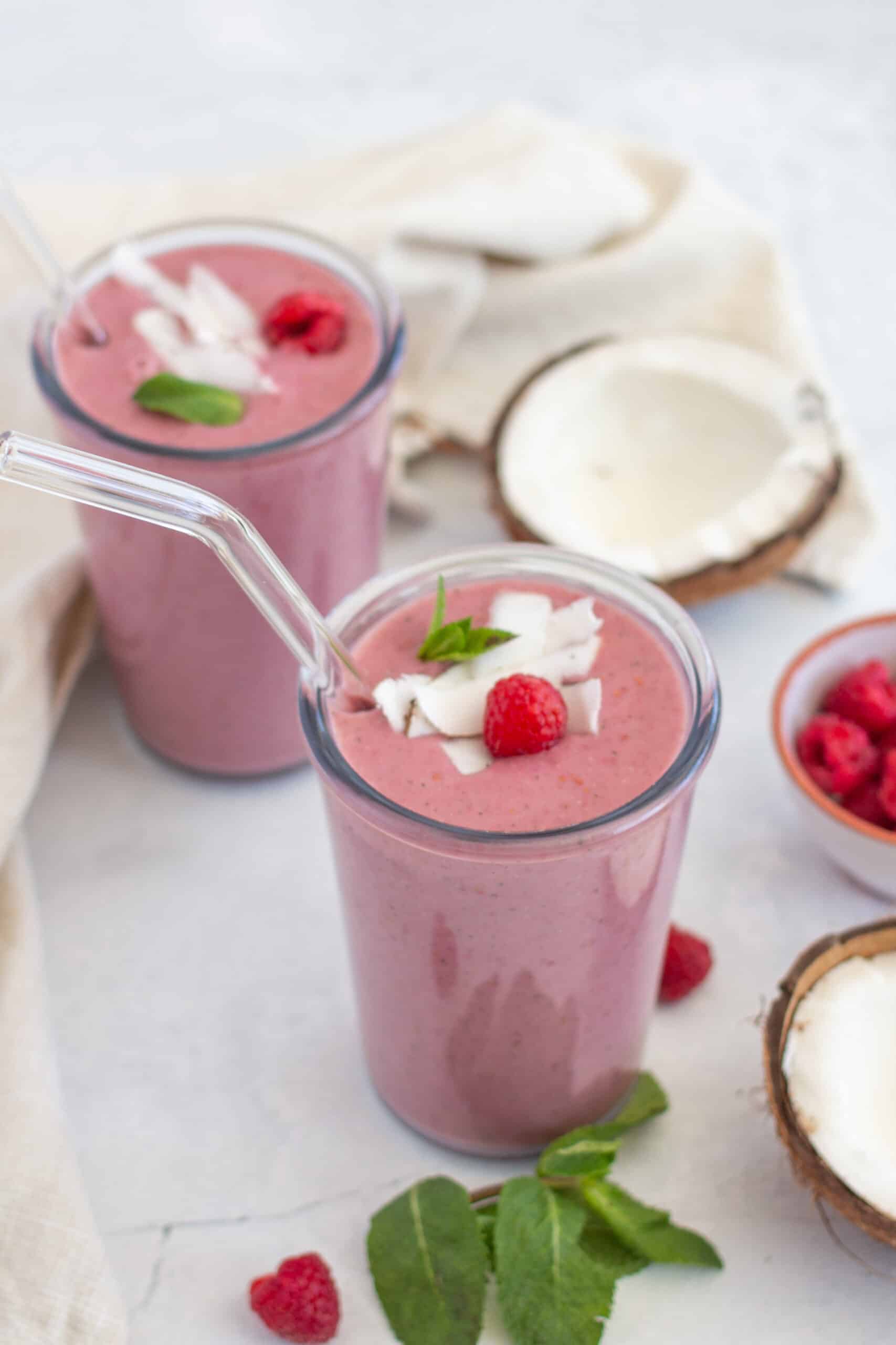 A red protein smoothie served in a glass with some fresh coconut in the background