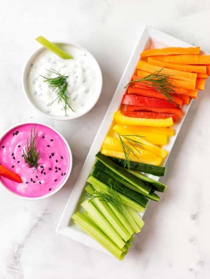 A white platter holding multiple vegetable sticks and two small bowls of dip on the side