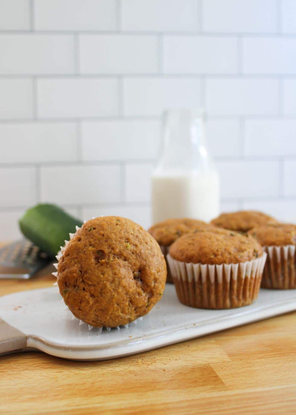 A zucchini muffin lying on its side on a white platter with a jug of milk in the background