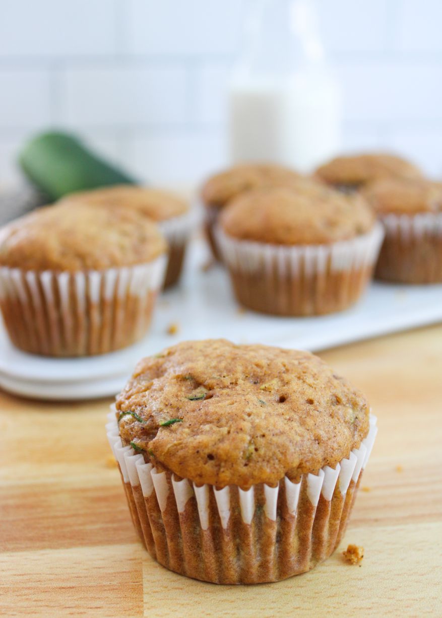 An up close shot of a muffin made with grated zucchini on a wooden bench with more muffins and a jug of milk in the background