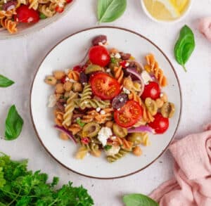 Chickpea pasta salad served on a white plate with fresh basil leaves and lemon on the side