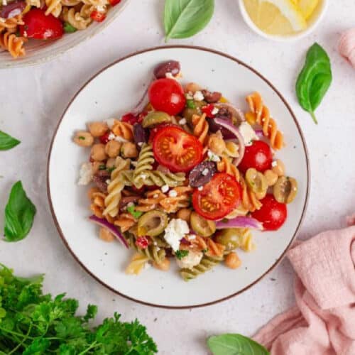 Chickpea pasta salad served on a white plate with fresh basil leaves and lemon on the side