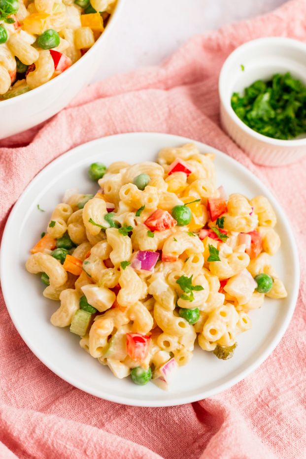 Macaroni vegetable salad served on a white plate with a pale pink linen underneath it
