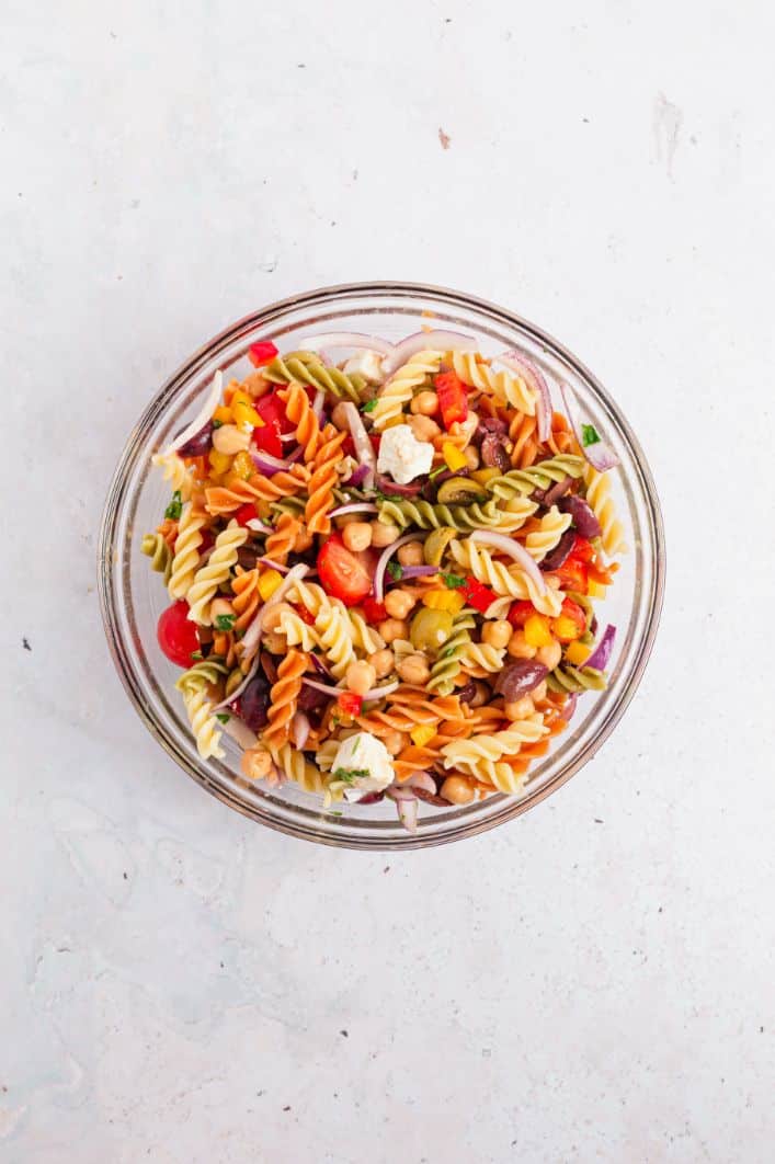 Overhead image of pasta, chickpeas, chopped veg and vinaigrette together in a glass bowl