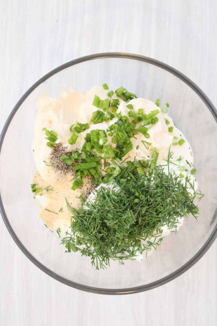 Mayo and sour cream in a large glass bowl and topped with fresh herbs