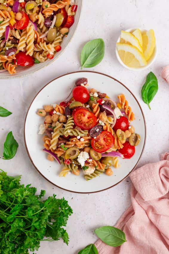 Overhead shot of a plate contained a Mediterranean chickpea pasta salad with some fresh lemons, basil and parsley in the background