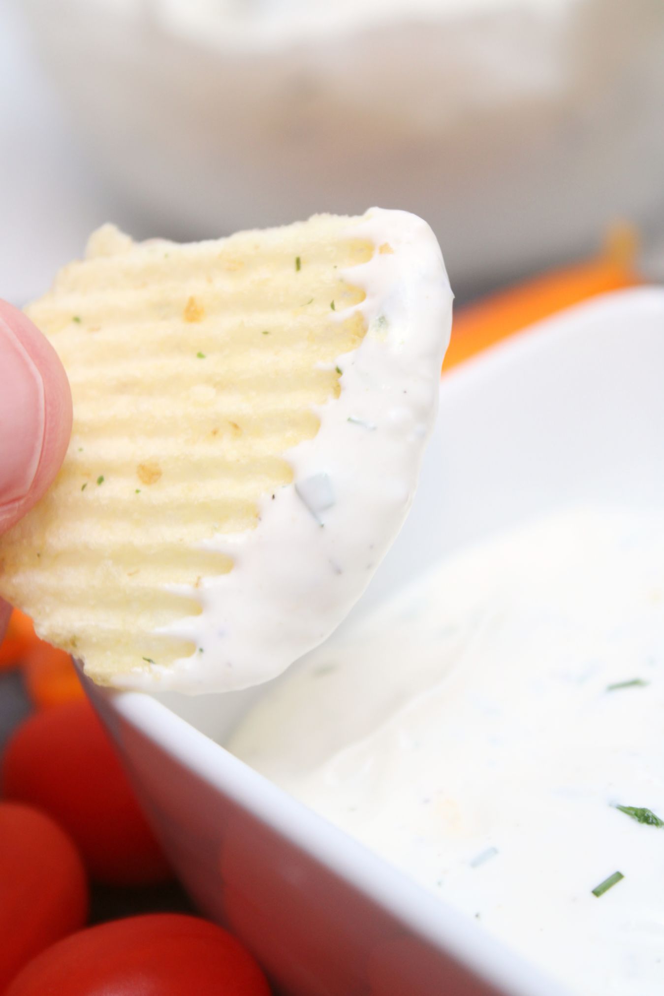 A chip being dipped into a white dip topped with fresh herbs