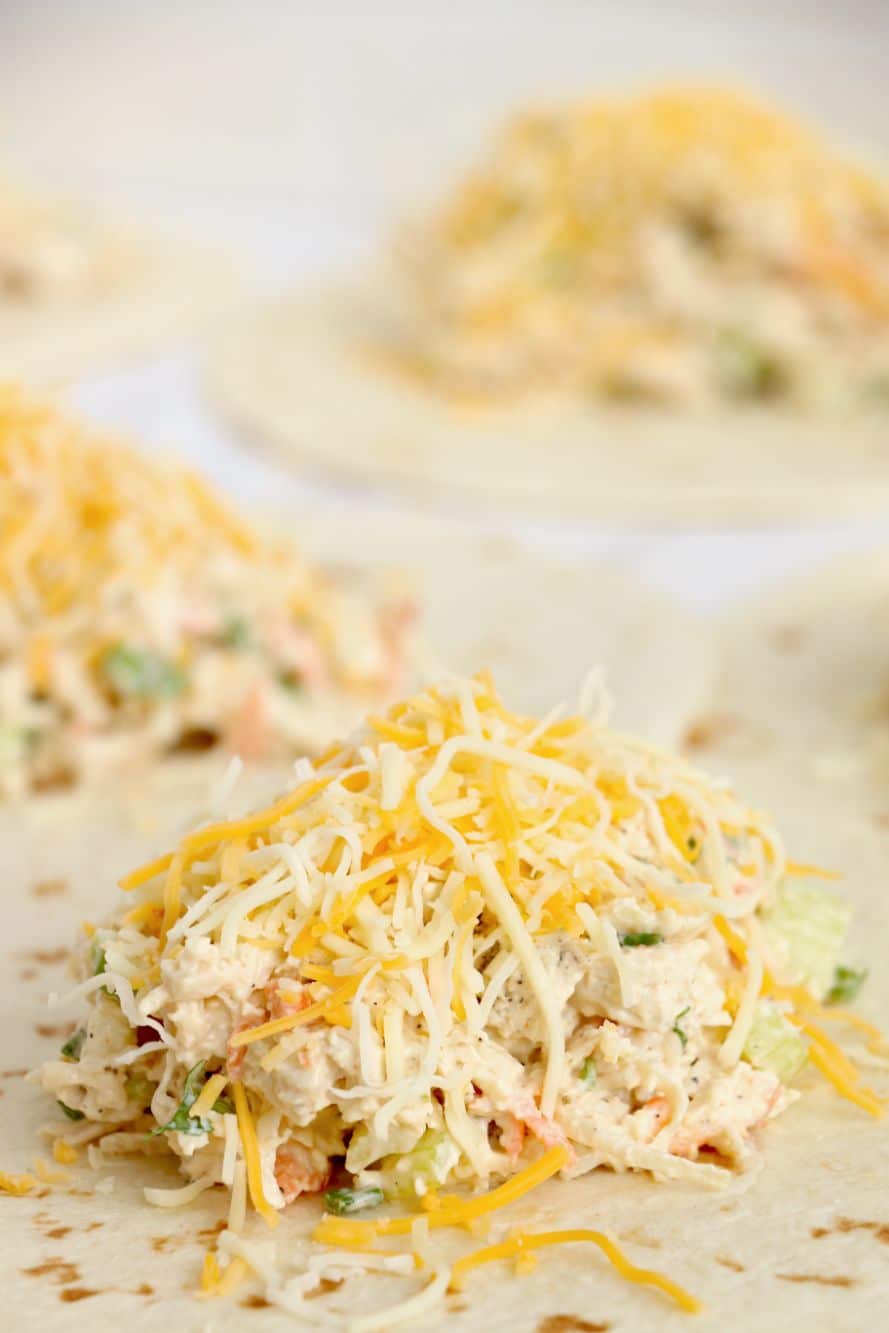 Cheese added to the top of a creamy chicken salad on top of a tortilla