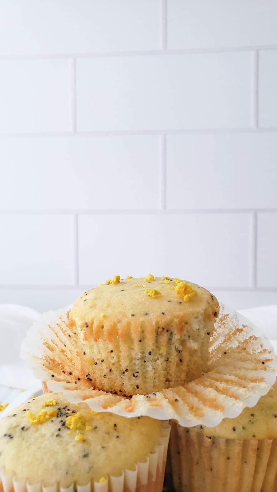 Up close shot of a bitten muffin stacked on top of two whole muffins with slices of lemon in the foreground
