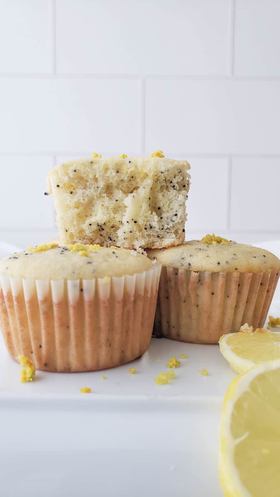 One bitten muffin stacked on top of two whole muffins with slices of lemon in the foreground