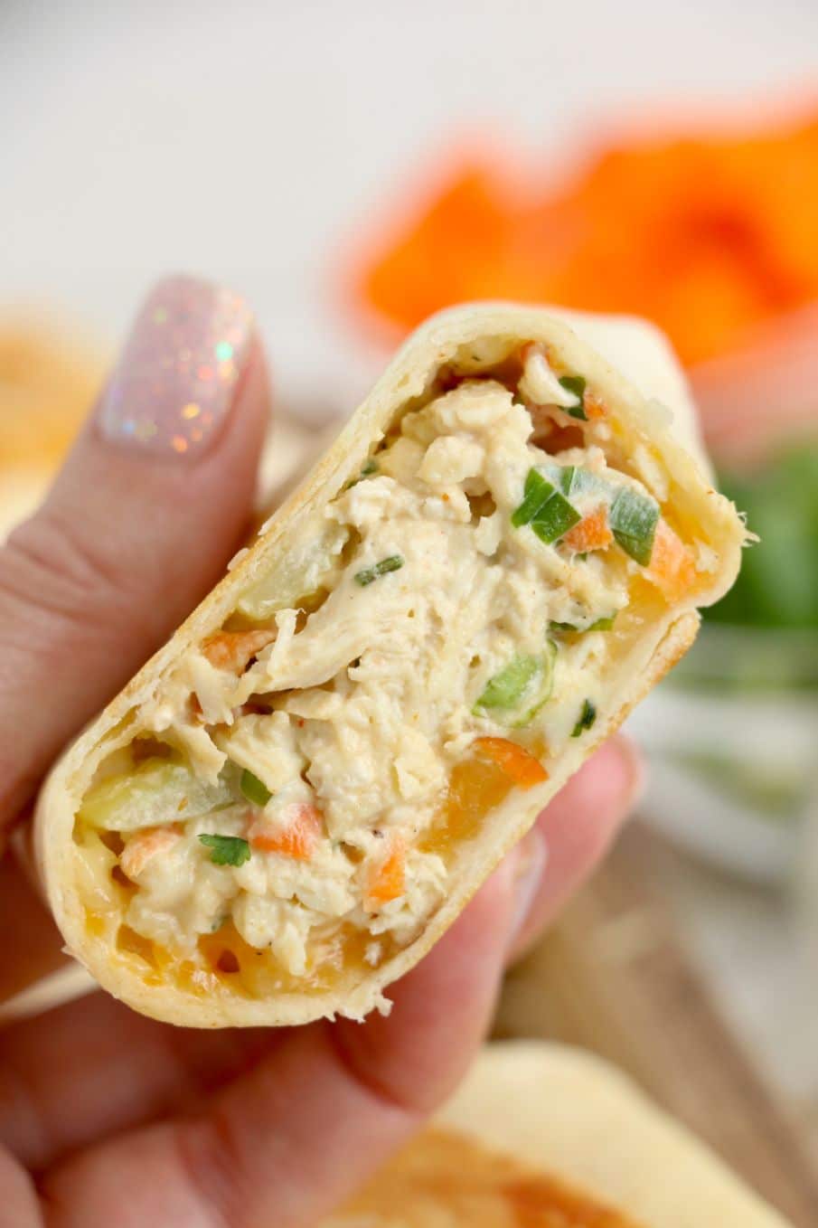 A chicken salad and cheese wrap cut in half and held by a hand