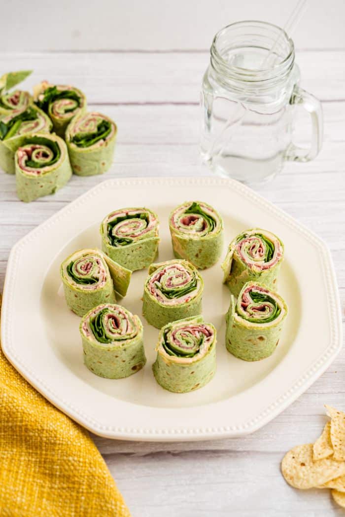 Wrapped spinach tortillas pinwheels served on a white plate with a cup of water
