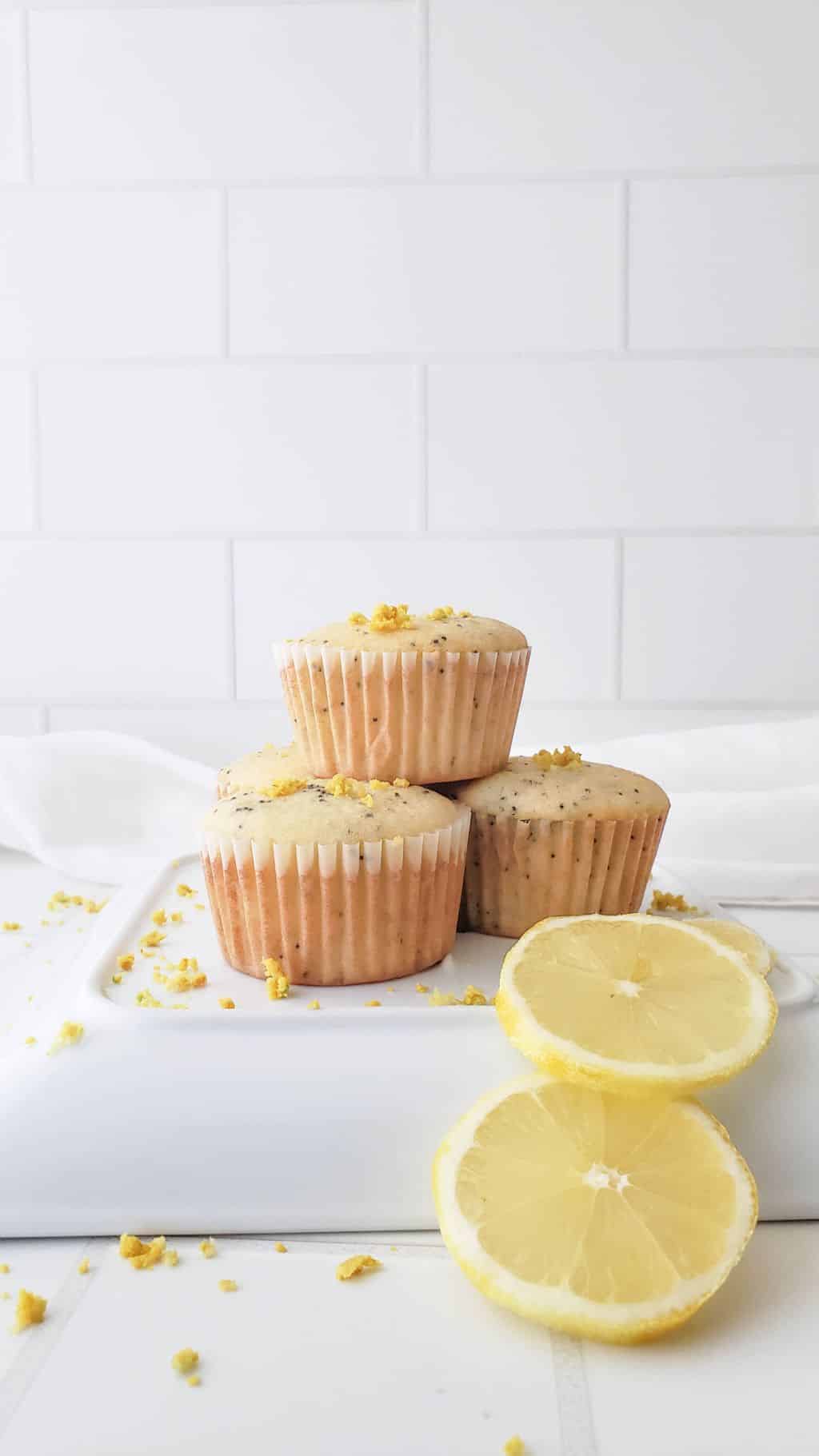 A stack of three lemon and poppy seed muffins on a white plate with slices of lemon