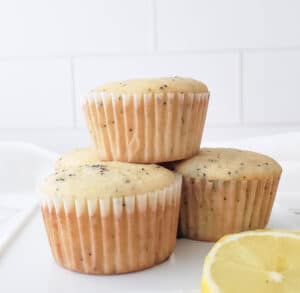 Three muffins stacked on a white plate with slices of lemon beside them