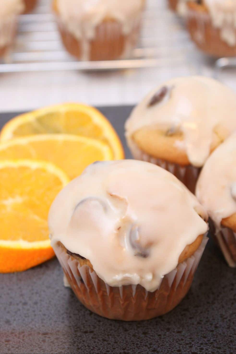 Glazed muffins served with orange slices. There are muffins cooling on a wire rack in the background