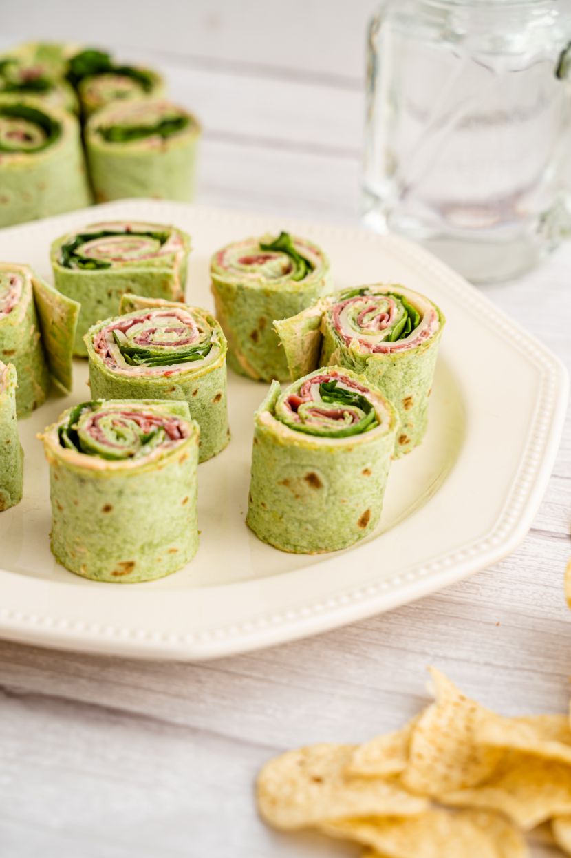 A couple of spinach roll ups wraps served on a white plate with a glass of water in the background