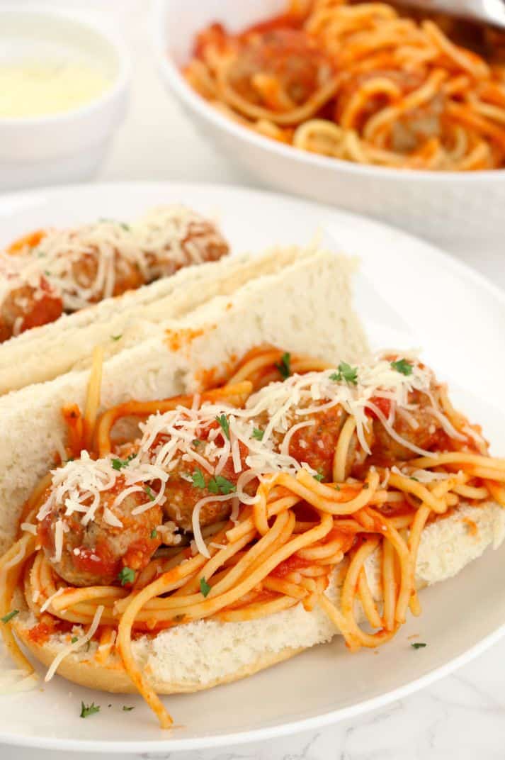 Mozzarella grated on top of a hotdog bun filled with meatballs, spaghetti and sauce