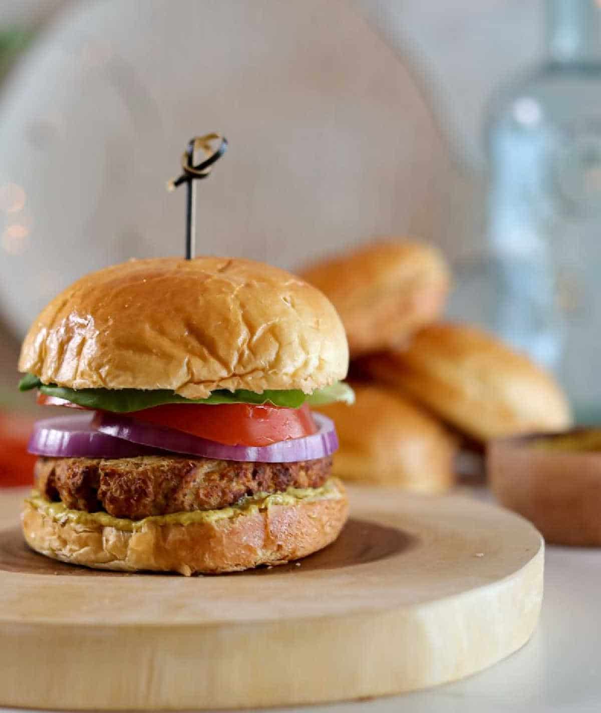 Tuna cakes stacked into a bun with some lettuce, tomato and red onion. A bamboo skewer is being used to hold it together.