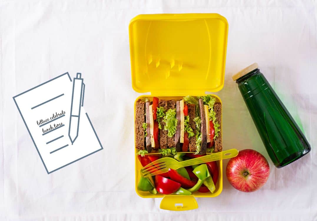 overhead shot of a yellow bento box with sandwiches, apple slices and a green juice