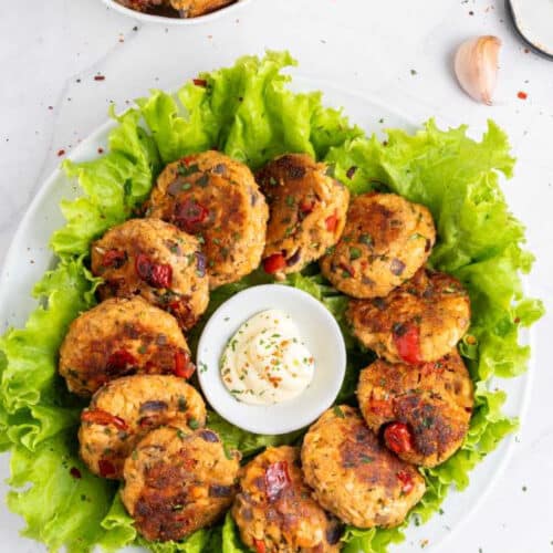 Crispy salmon bites arranged in a circle in a white bowl on top of lettuce leaves with a bowl of mayonnaise in the middle