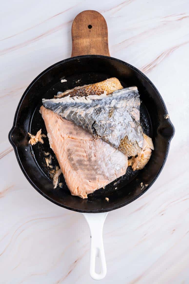 Cooked salmon in a black skillet with the skin pulling away easily