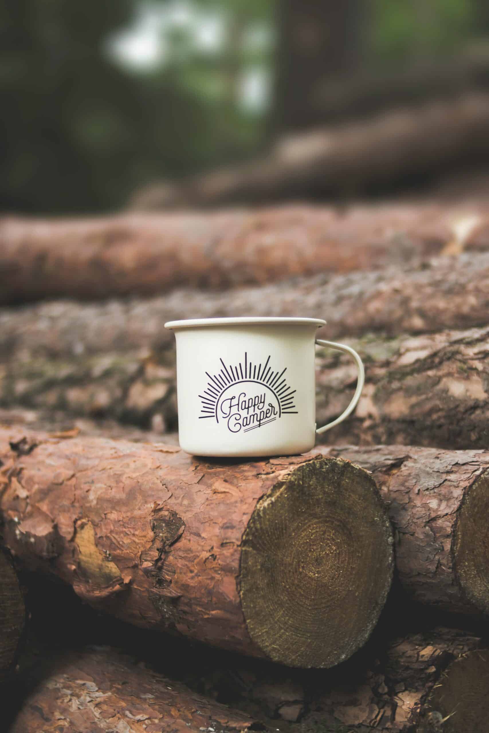 White colored happpy camper mug resting on top of some logs