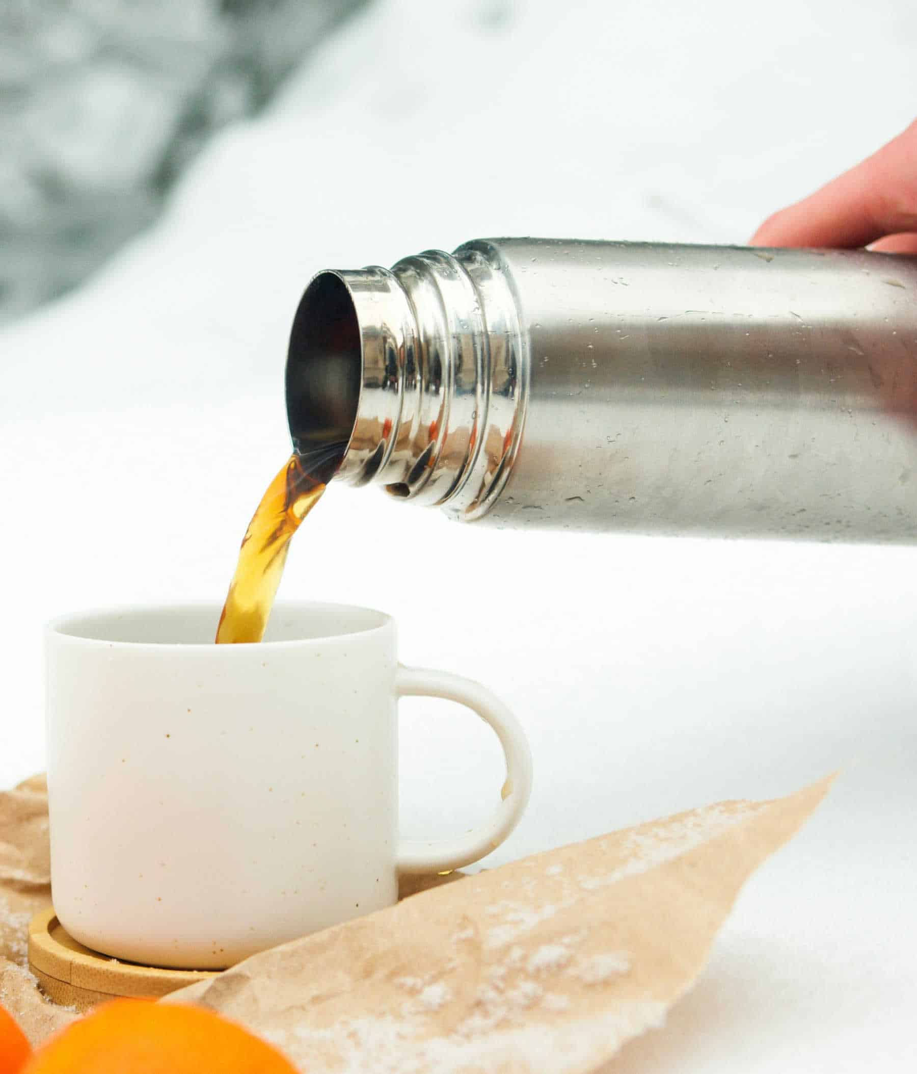 Thermos pouring hot tea into a white cup against a white background