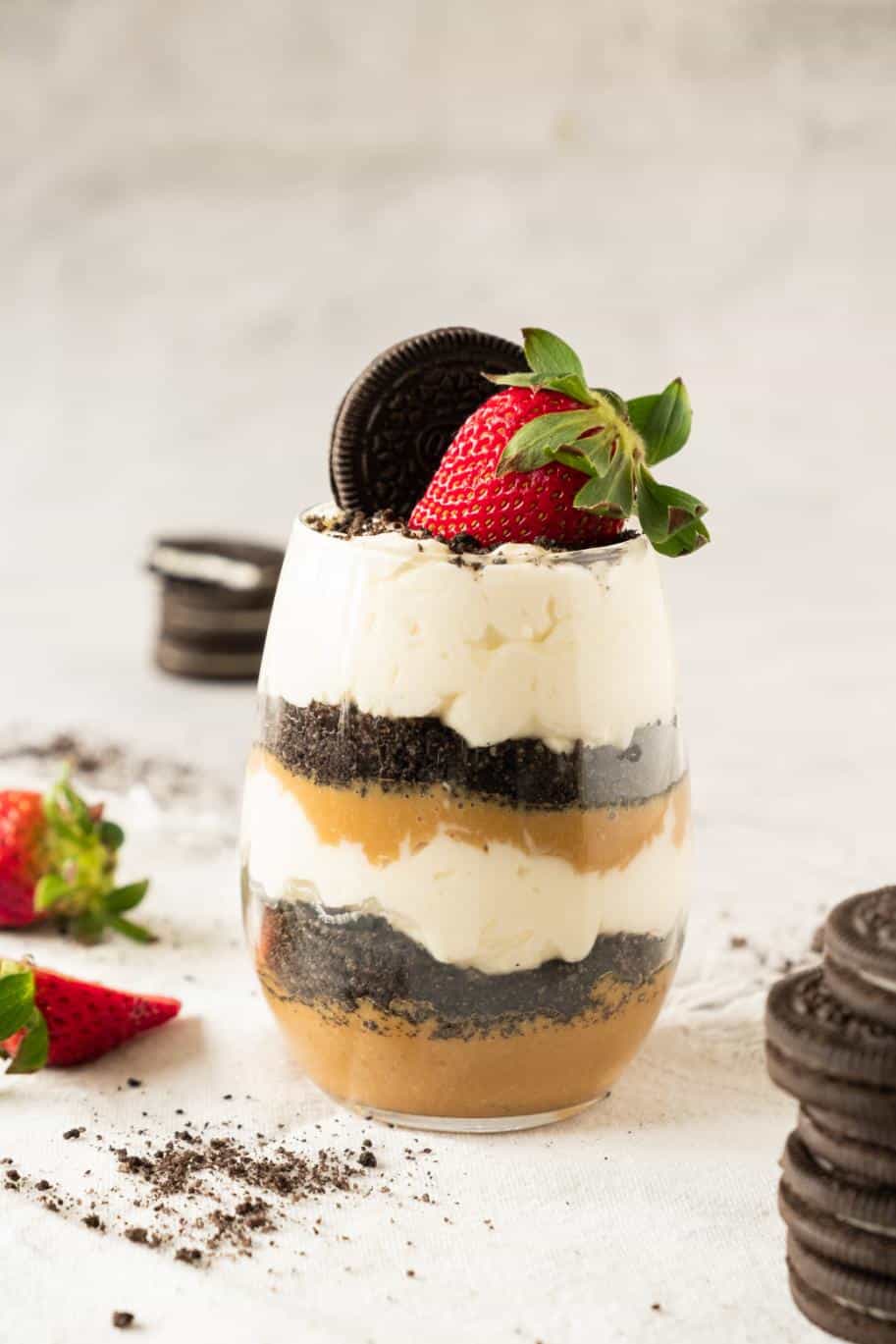 Oreo dirt pudding parfait layered in a tall glass and topped with a whole oreo and a strawberry