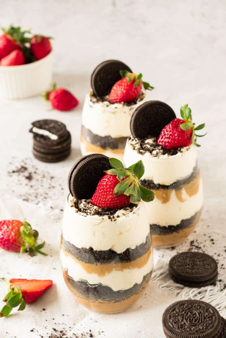 Three glasses full of layered oreo desserts and topped with a whole oreo and a strawberry